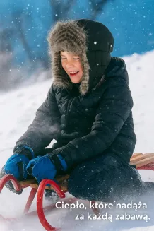 Dziecko (5-8 lat) w czarnej czapce pilotce W-151K, zabawa w śniegu, czapka wodoodporna, ciepła, z futerkiem, pewne zapięcie pod szyją, radość z zabawy.